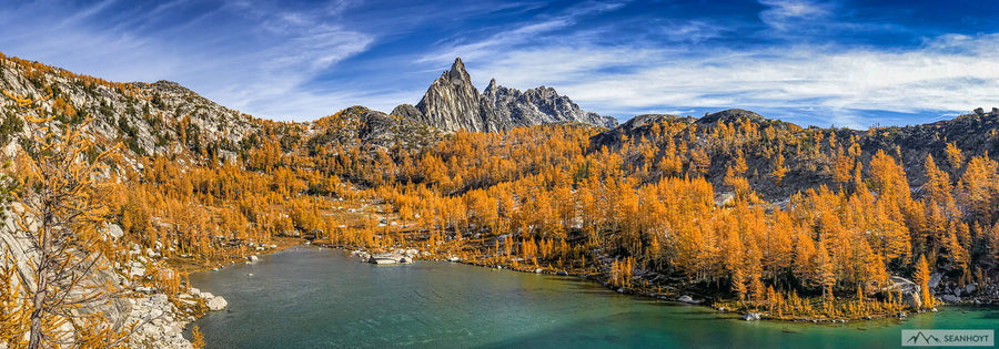 a view from above a green lake with golden larch trees filling the valley beyond and a jagged peak protruding in the distance